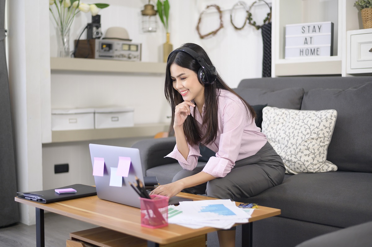 A beautiful young woman wearing headset is making video conference call via computer at home , business technology concept .