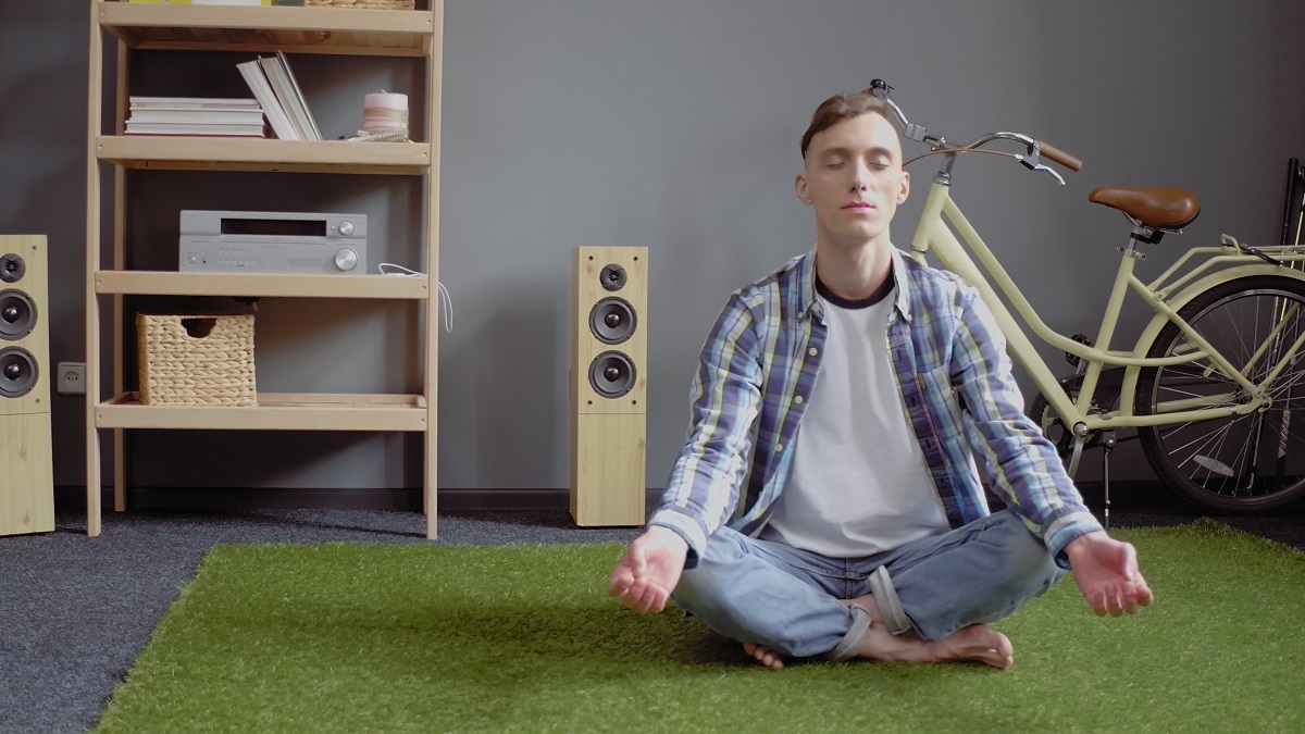 Caucasian man meditates resting closed eyes while sitting crossed legs on green carpet. Self-isolation at home. Quarantine concept. Toned image